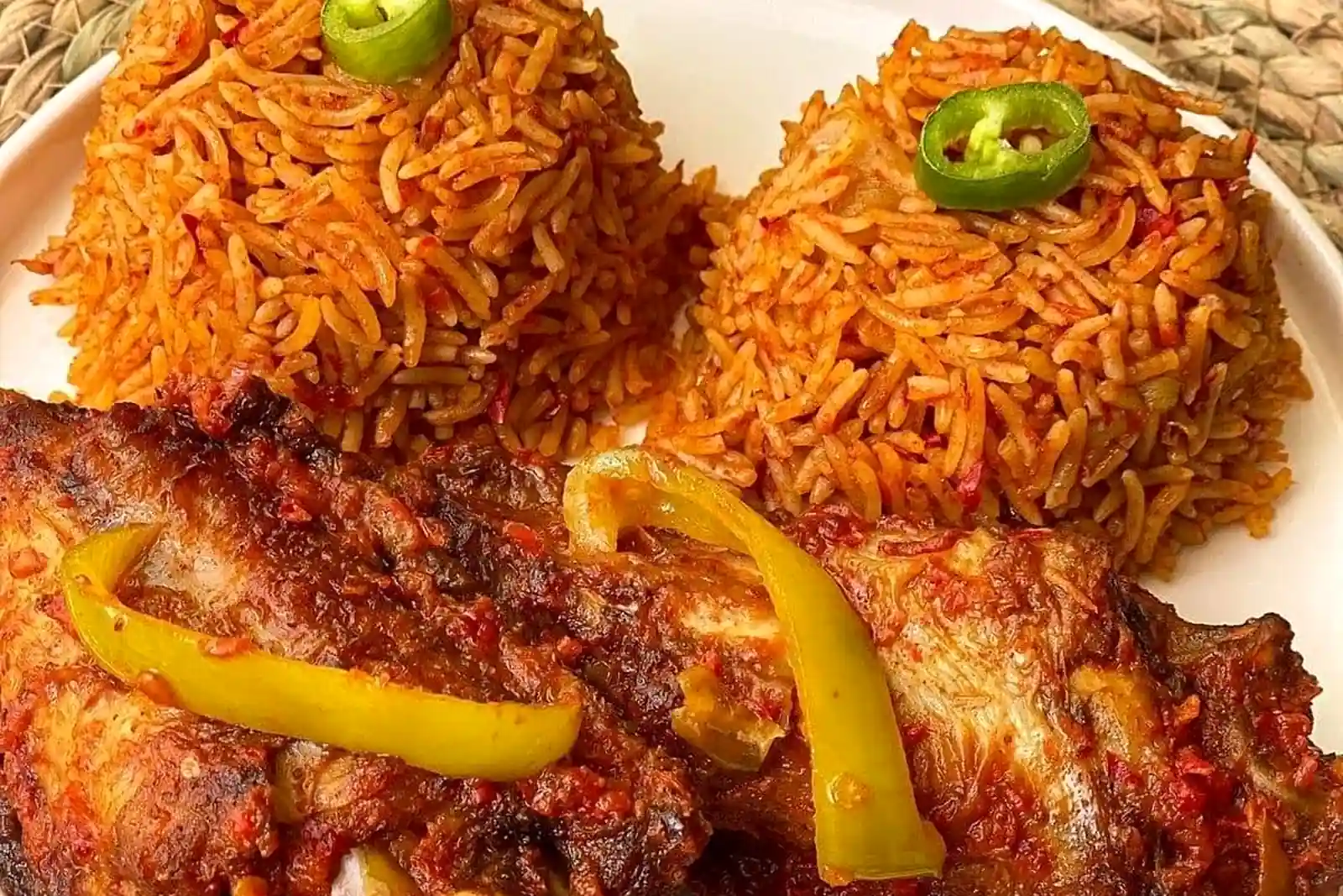 Two portions of red-orange jollof rice with richly seasoned grilled chicken and yellow pepper